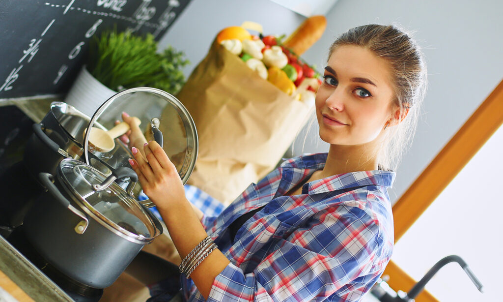 Kvinna står vid en spis och lyfter locket till en kastrull