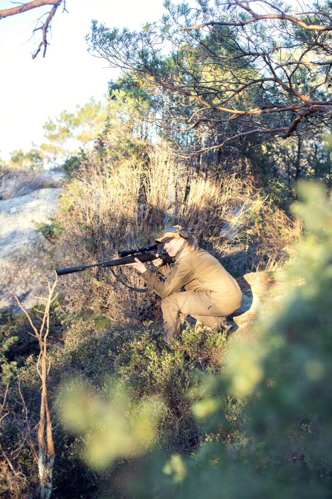 Jägare i skogsmiljö siktar med gevär under en solig dag.